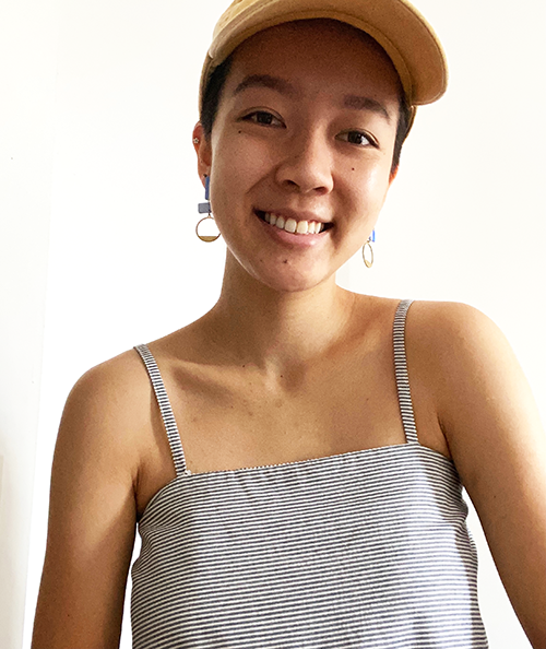 Mai is indoors smiling. She is wearing a cap and there is a white wall behind them.